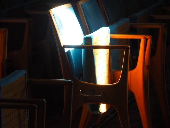 Ein Stuhl in einer Stuhlreihe, der besonders vom einfallenden Licht beleuchtet wird