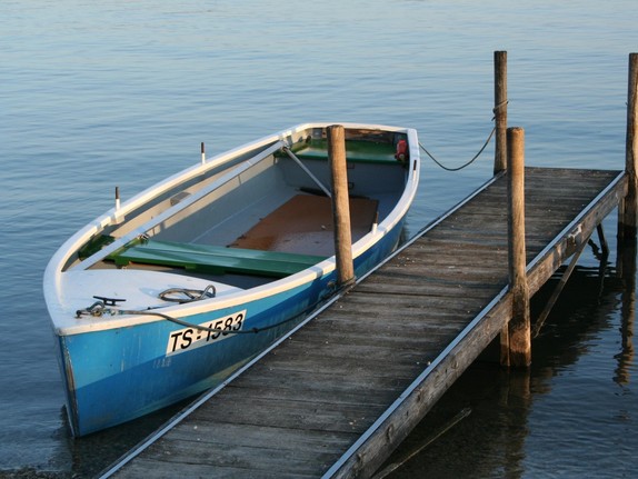 Zu sehen ist ein leeres Ruderboot, festgeknotet an einem Steg
